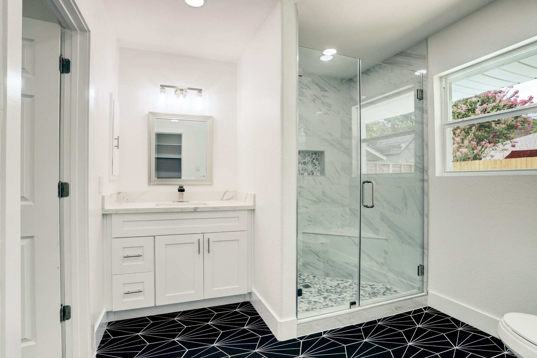 Bathroom remodel with frameless glass shower and geometric black floor tile